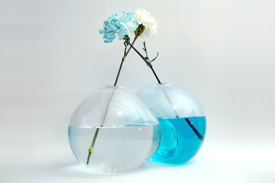 two blown glass vases with flowers propped up in a blue solution