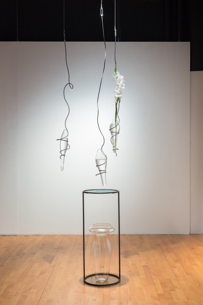 installation view of suspended blown glass sculptures and flower